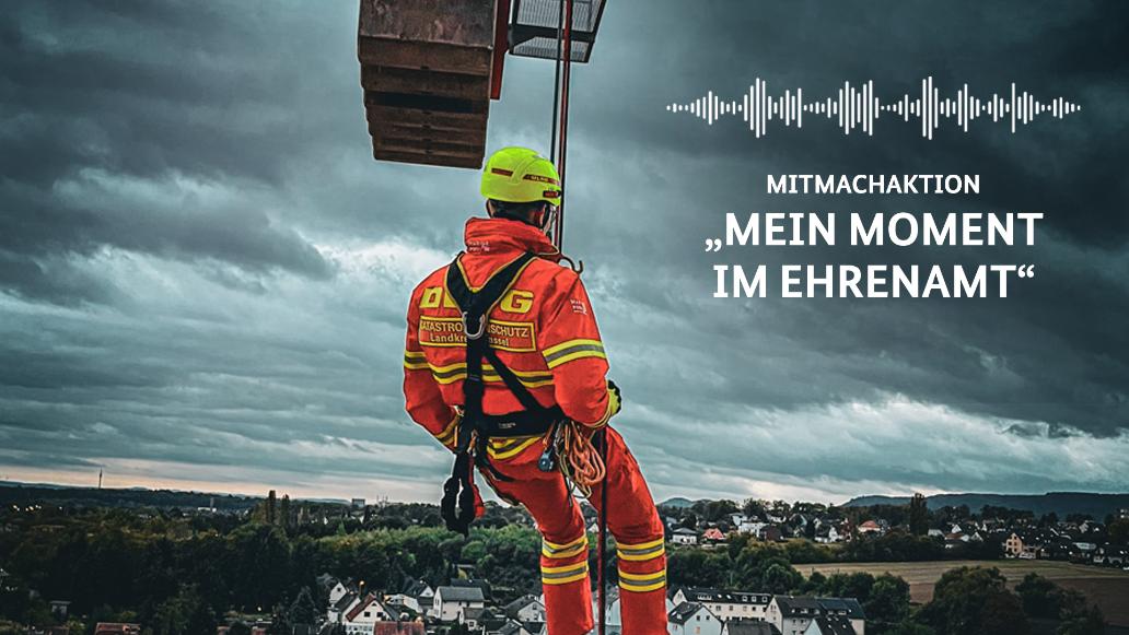 Mitmachaktion: "Mein Moment im Ehrenamt". Ein DLRG-Mitglied in voller Sicherheitsausrüstung blickt hinunter auf eine Stadt. Plakat.
